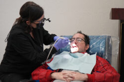 ACRC individual Adams sits in a dentist chair while a dentist staff member cleans his teeth.